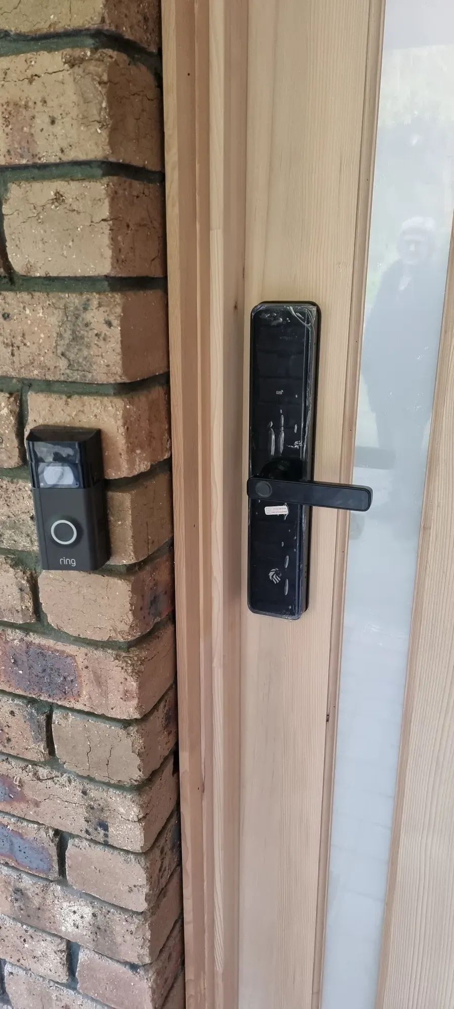 A smart lock beside a video doorbell on a brick wall